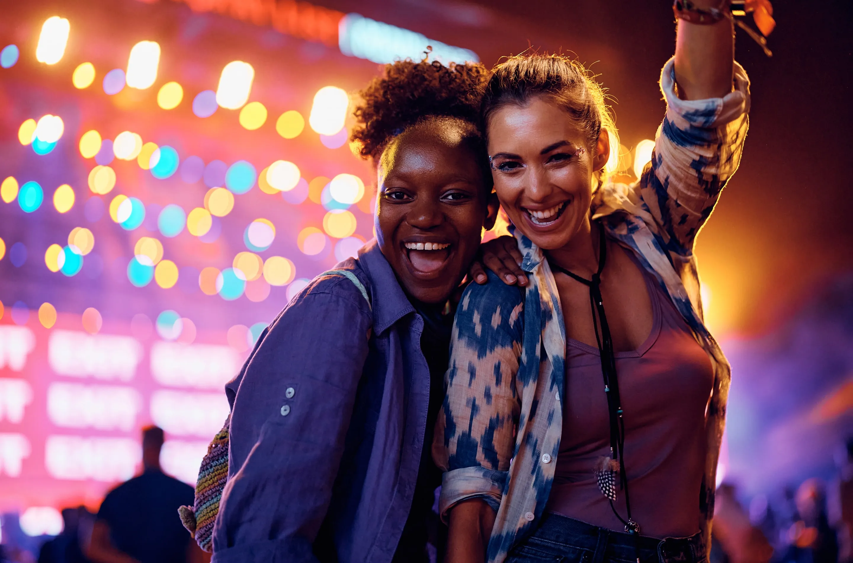 Two women smiling and enjoying a night out with colorful bokeh lights in the background.
