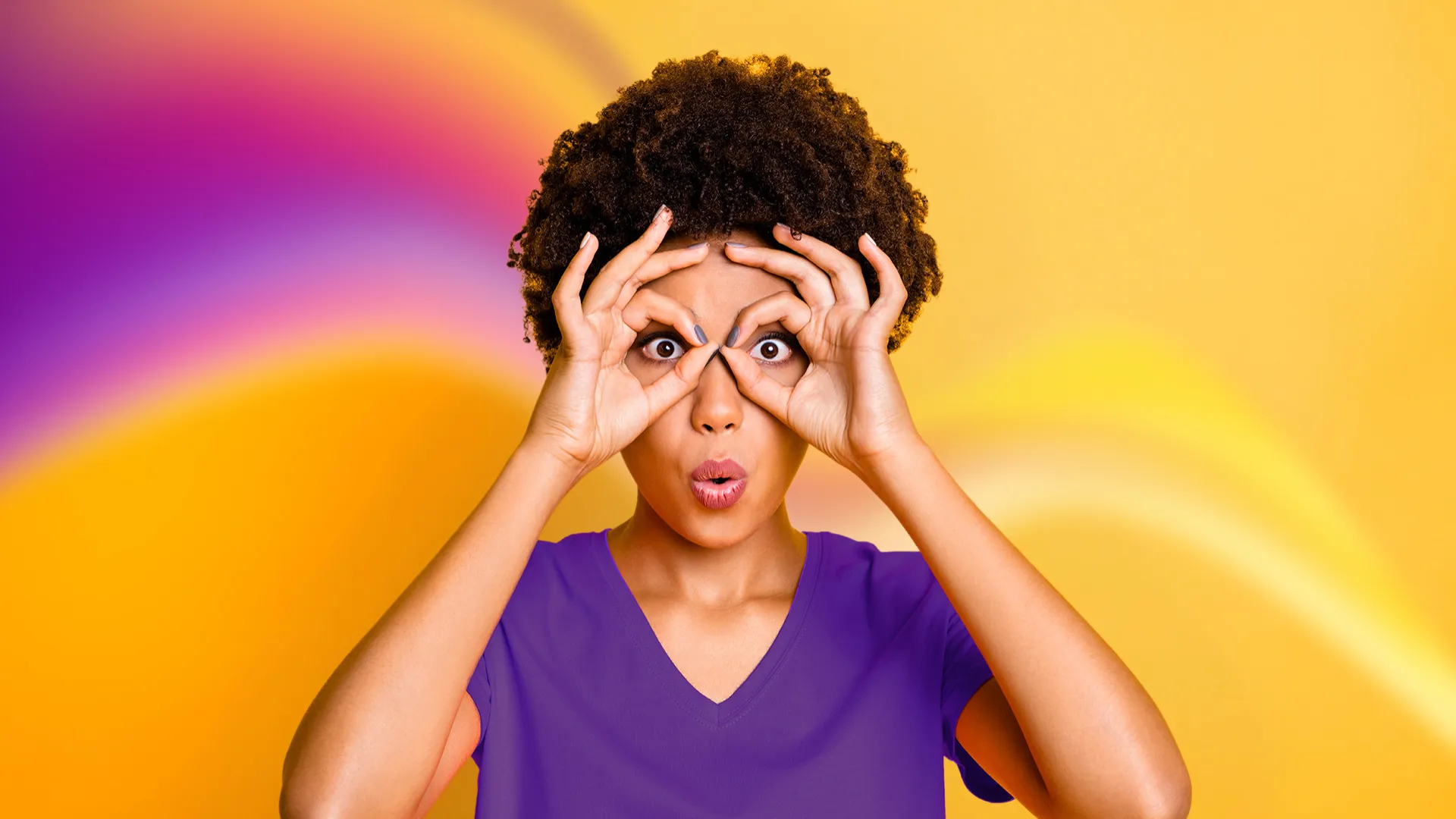 Woman with curly hair making binoculars with her hands and wide eyes, against a vibrant orange and purple background.