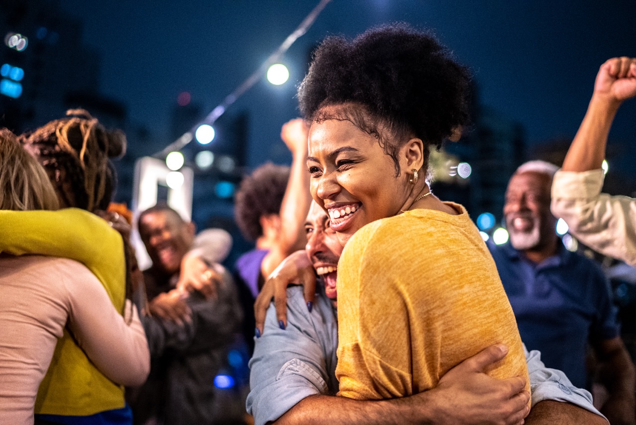 Group of diverse people joyfully hugging and celebrating together outdoors at night.