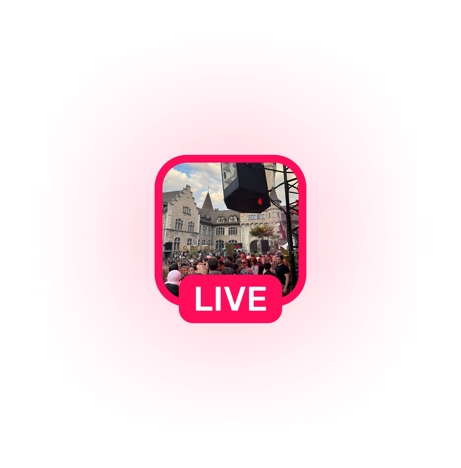 Crowd gathered at an outdoor live event in front of historic stone buildings with a blue sky and clouds.