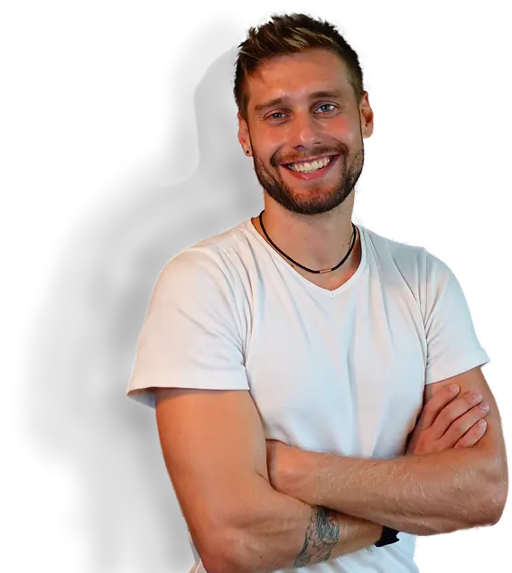 Lächelnder junger Mann mit kurzem Bart und Tattoos trägt weißes T-Shirt und verschränkte Arme vor schwarzem Hintergrund.