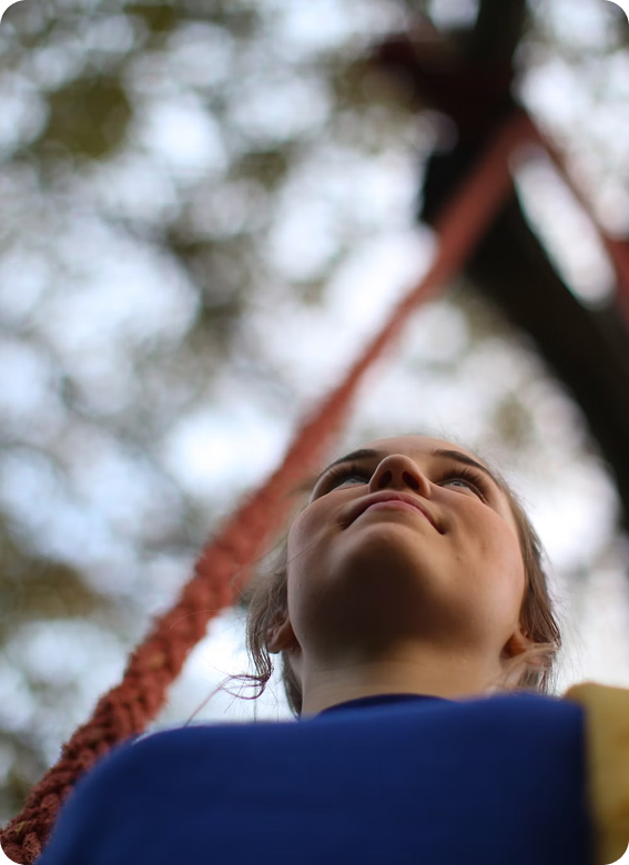 Low-angle view of a woman looking slightly upwards outdoors with blurred tree branches and a red rope in the background.