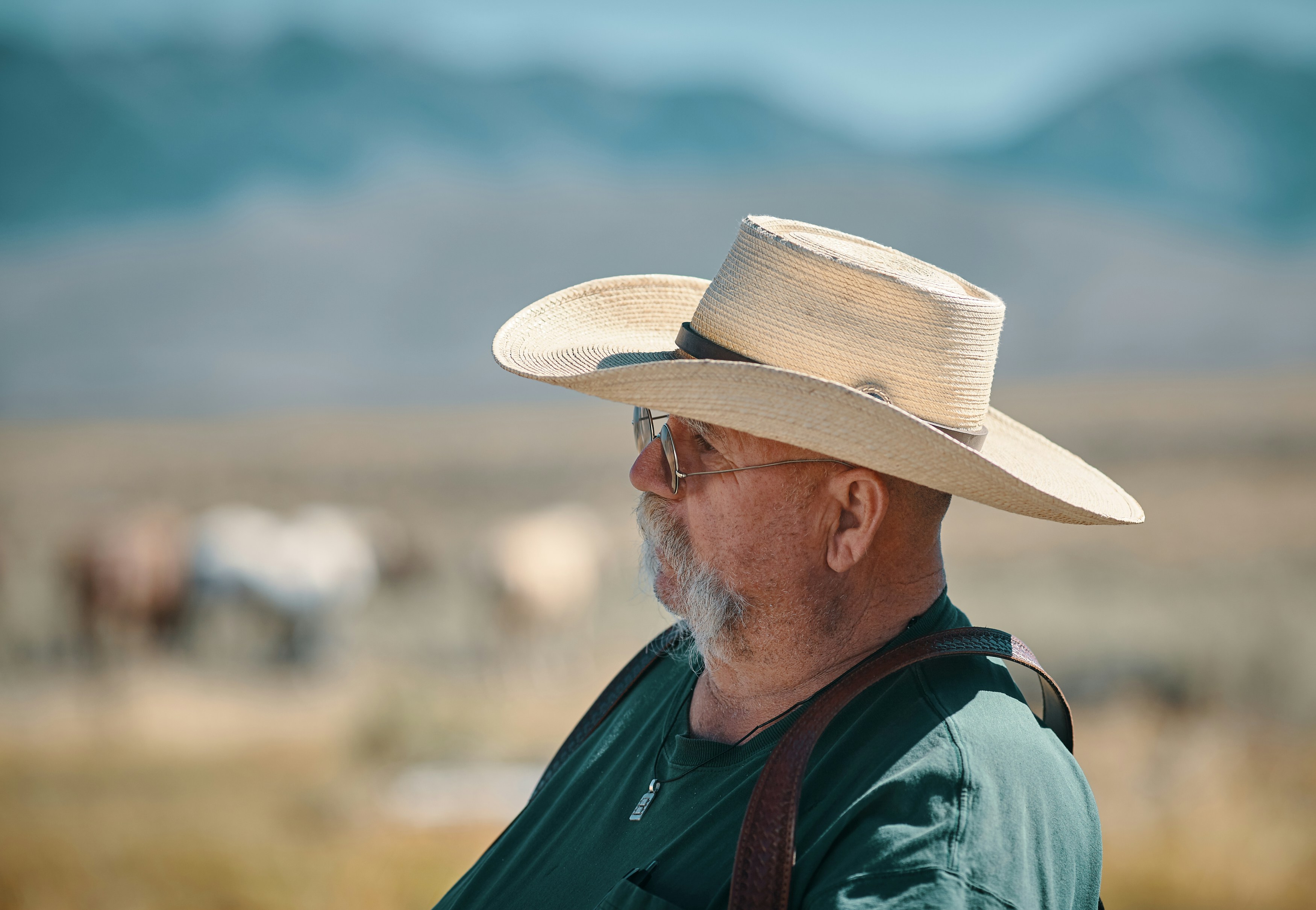 Side profile of an older man wearing a wide-brimmed straw cowboy hat and sunglasses in an outdoor rural setting.