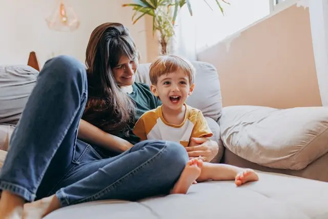Smiling woman and young boy sitting on a couch in a bright living room.