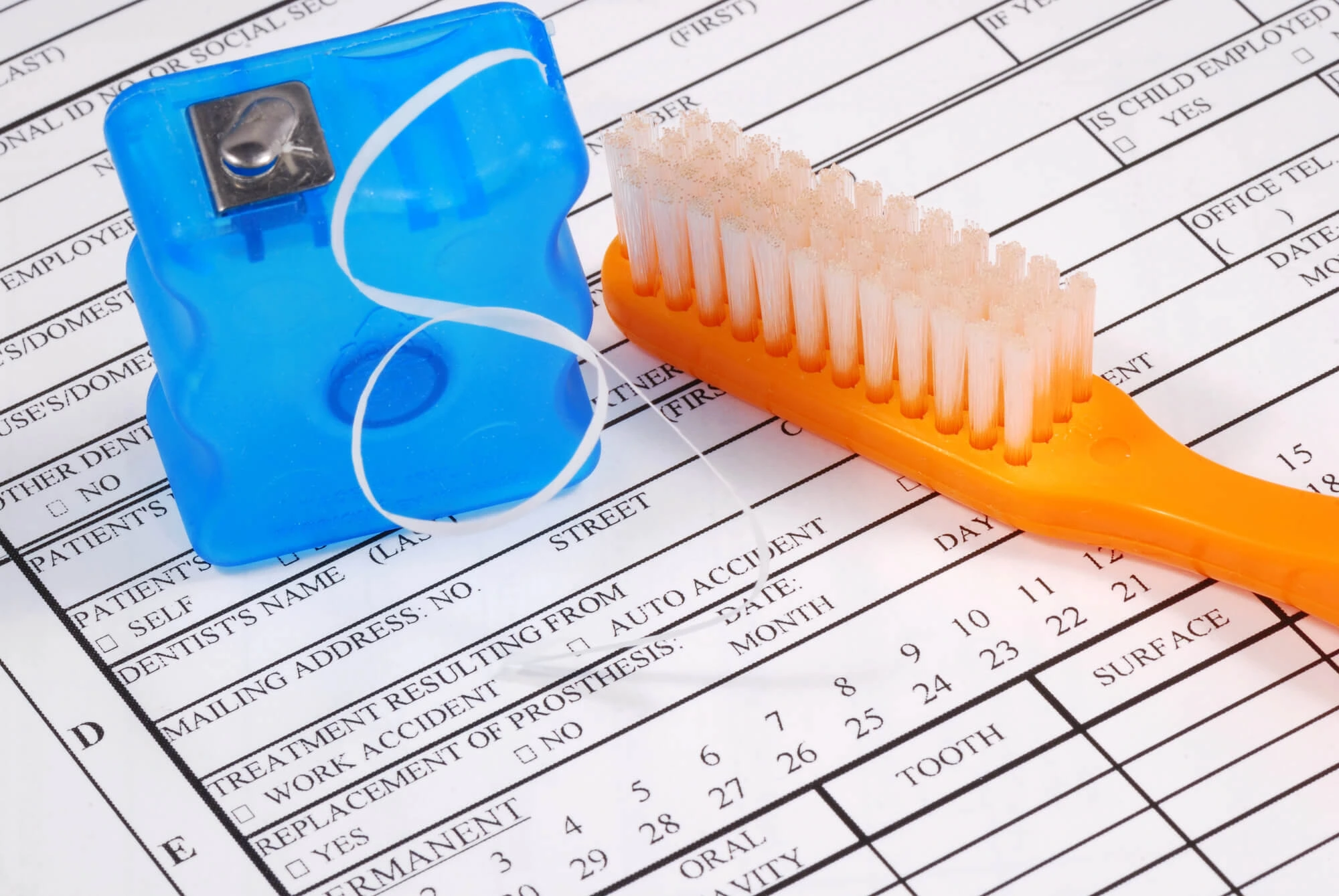 Dental floss container and orange toothbrush on top of a printed dental patient form.