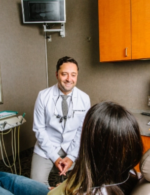 Smiling dentist in white coat talks to a female patient in a dental clinic room.