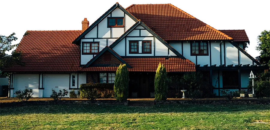 Großes Haus im Tudor-Stil mit weißen Wänden, braunen Holzbalken und rotem Ziegeldach bei Sonnenlicht.