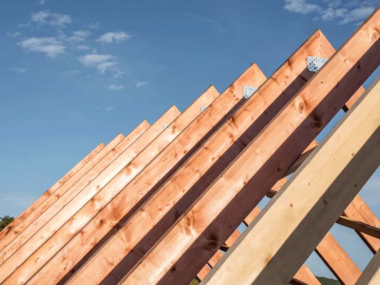 Holzrahmen einer Dachkonstruktion unter klarem blauem Himmel.