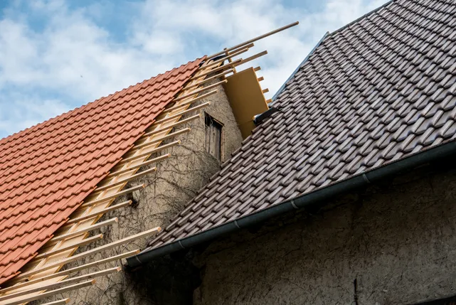 Dachsanierung detmolod friesen dach: Teilweise eingedecktes Satteldach mit neuen roten Dachziegeln neben einem alten mit braunen Dachziegeln unter bewölktem Himmel.