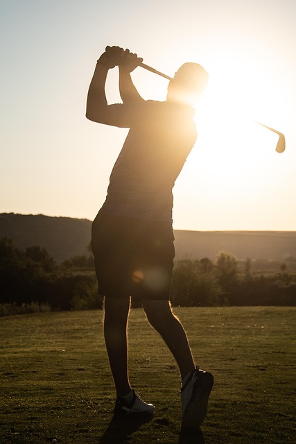 Silhouette of a person swinging a golf club on a grassy field at sunset.