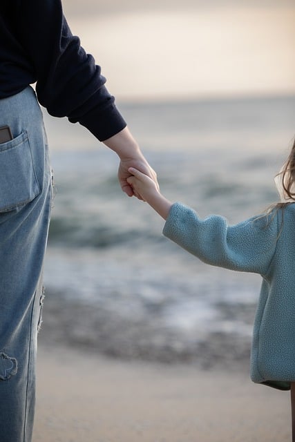 Adult and child holding hands by the seashore with blurred ocean background.