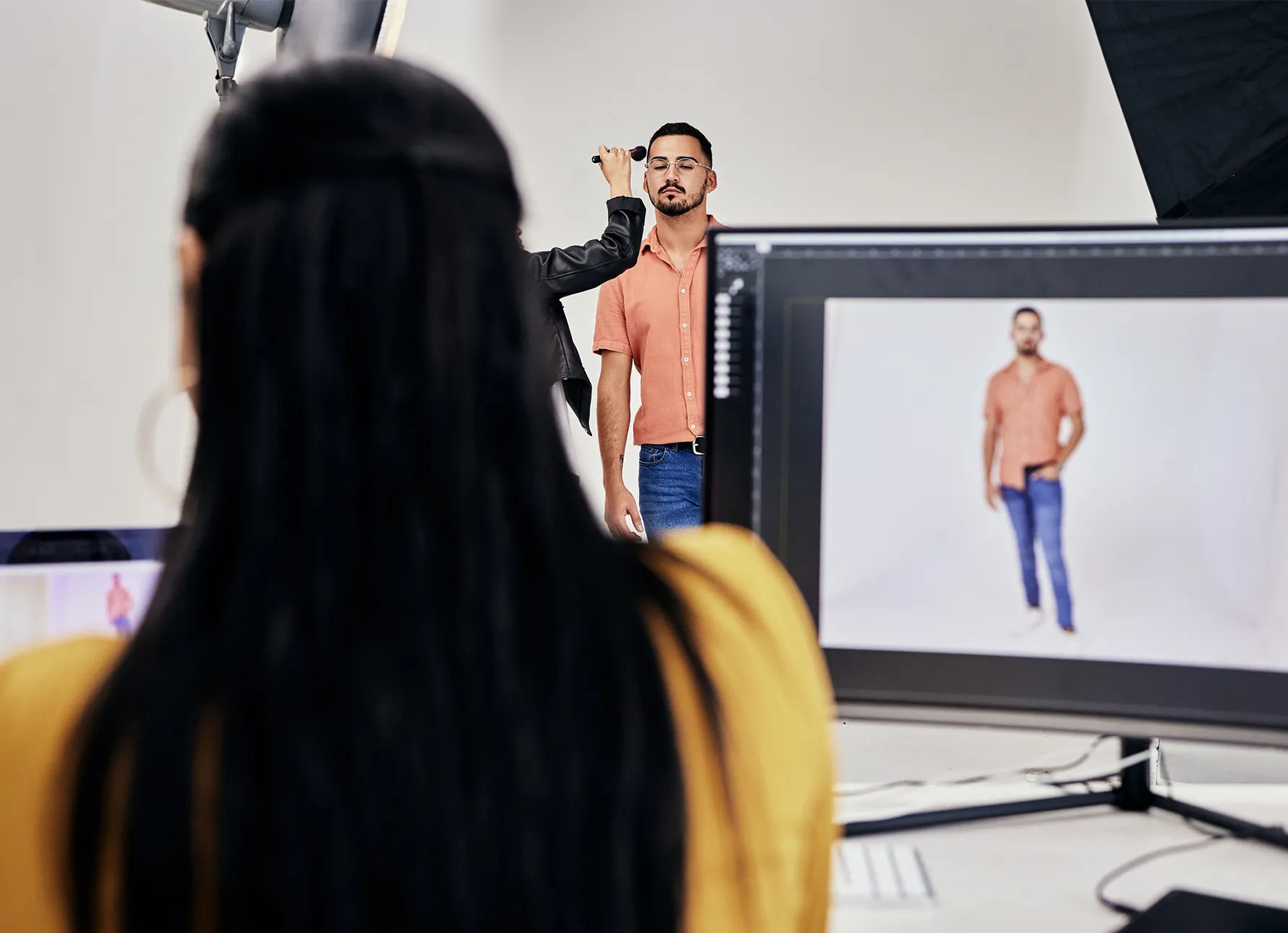 A male model being applied some make up finishing touches in a studio. On the screen it appears that there is an image on Capture One