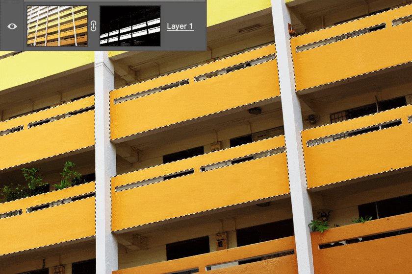 Yellow apartment building with horizontal railings and some green plants, with a Photoshop layer mask interface overlay in the corner.