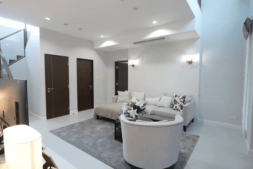 Modern living room with a light grey sectional sofa, round beige chair, gray area rug, and three brown doors visible near a staircase.