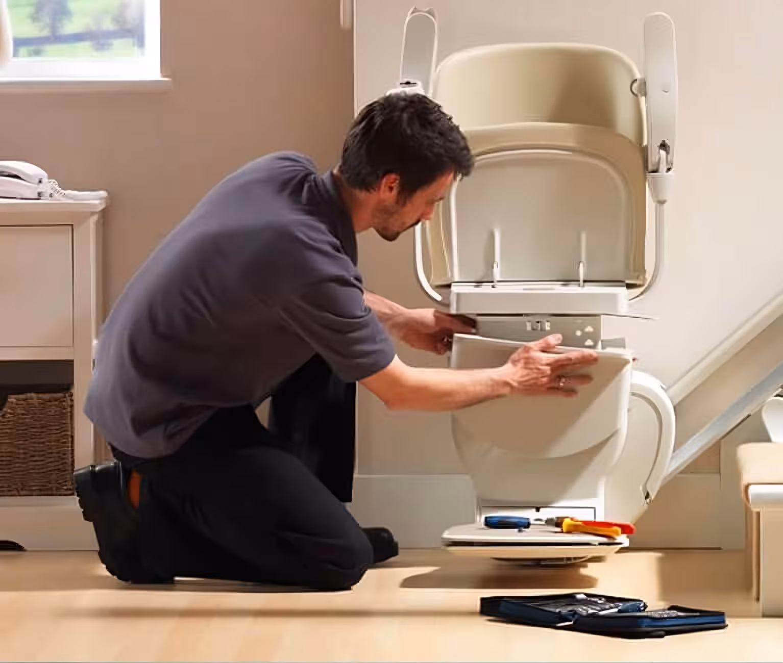 Service technician working on a stairlift installation with tools on the floor.