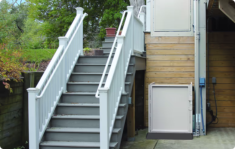 Outdoor staircase with white railings next to a wooden building featuring a wheelchair lift.