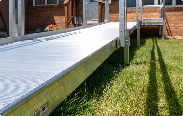 Close-up of a metal wheelchair ramp leading up to a house entrance with green grass beside it.