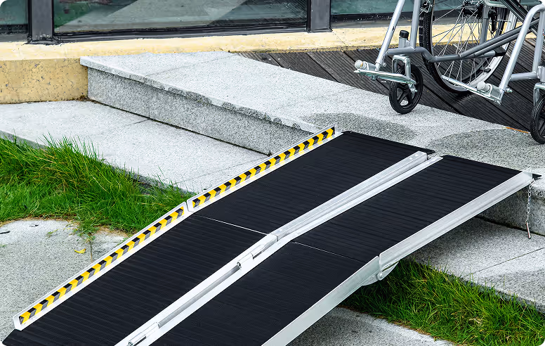Portable wheelchair ramp placed against steps beside a bicycle, leading from pavement to elevated doorway.
