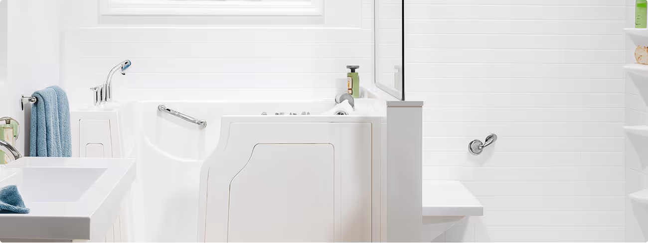 Bright white bathroom featuring a walk-in bathtub with grab bars, a white sink with a blue towel, and white tiled walls.