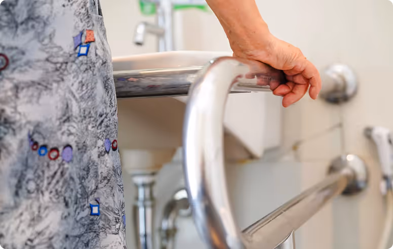 Person holding a metal support rail near a sink in a bathroom.
