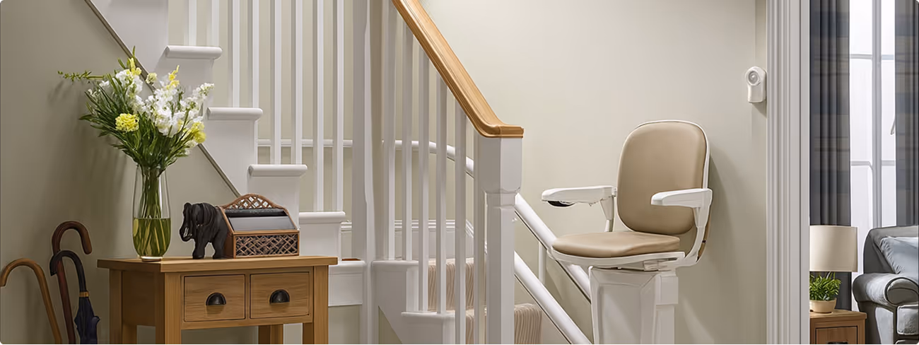 Staircase with beige stair lift chair and wooden side table with flower vase and decorative items.