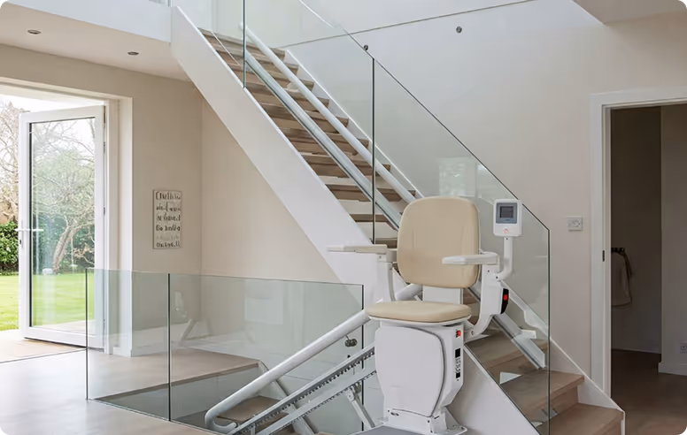 Modern home interior with a beige stairlift attached to a staircase with glass railings and an open door leading to a garden.