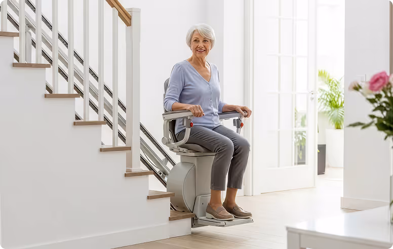 Elderly woman sitting on a stairlift at the bottom of a staircase in a bright home interior.