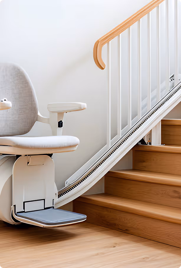 Modern stairlift with padded seat and footrest installed on wooden stairs with white railing.