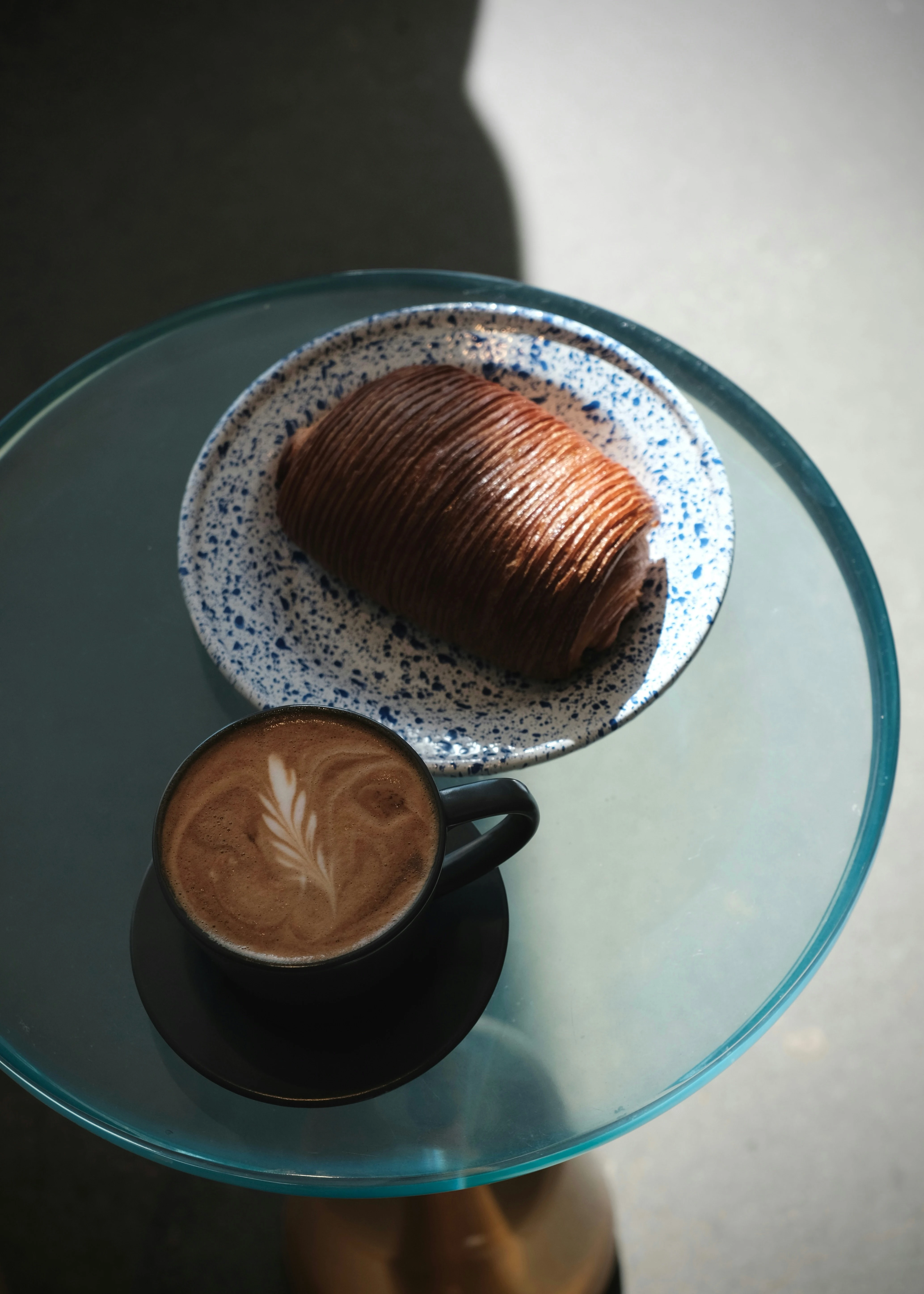 En fikastund med kaffe och bulle på ett blått cafébord.