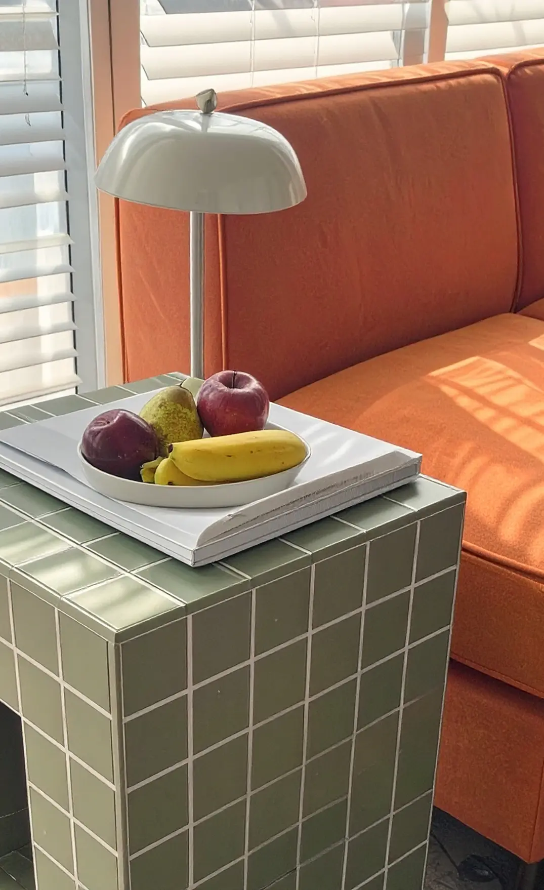 En fruktskål med bananer, äpplen och päron på en piedestal i fin och mysig kontorsmiljö.