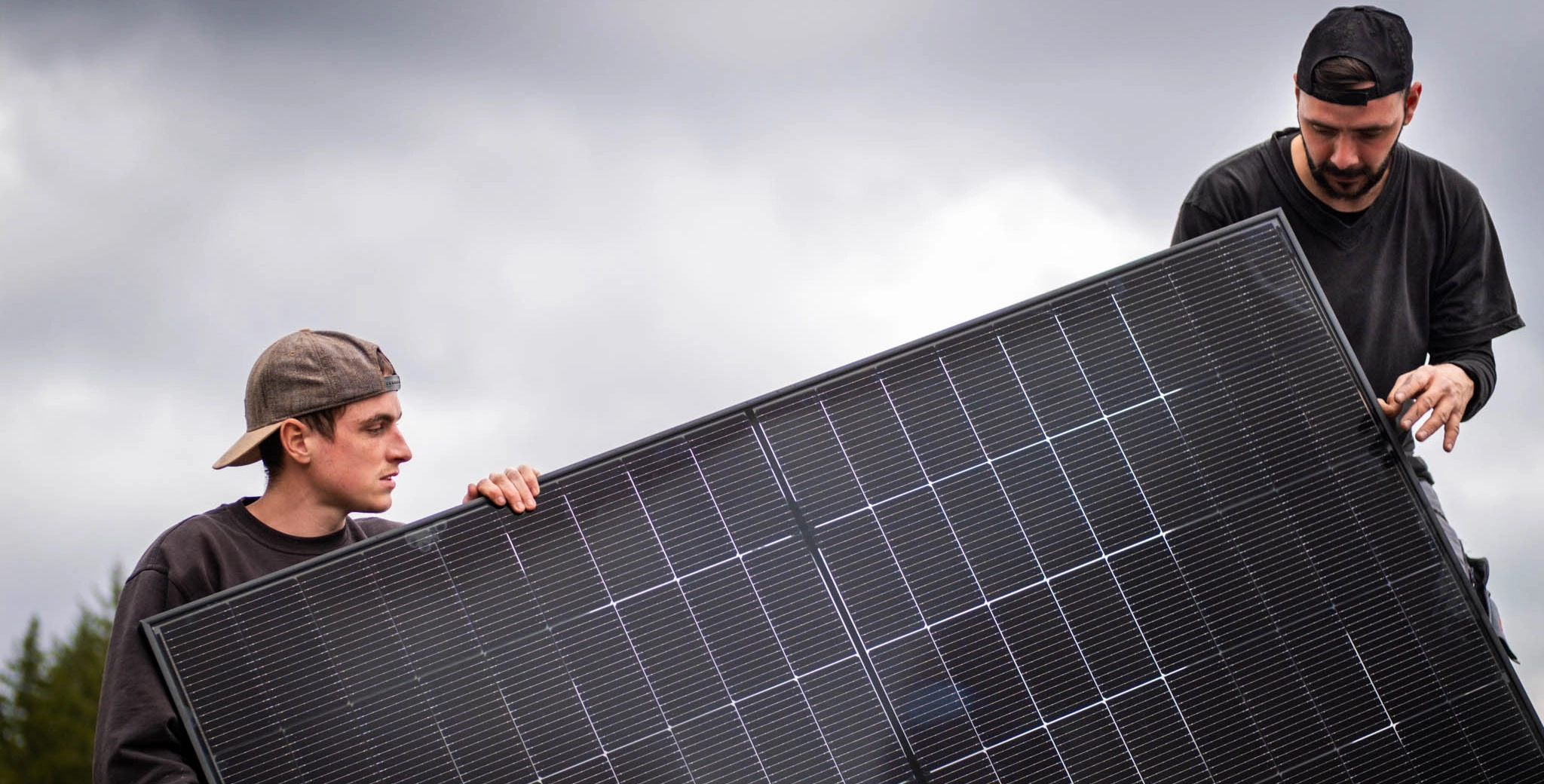 Monteur für Photovoltaik-Anlagen sitz auf einem Dach vor einem PV-Modul