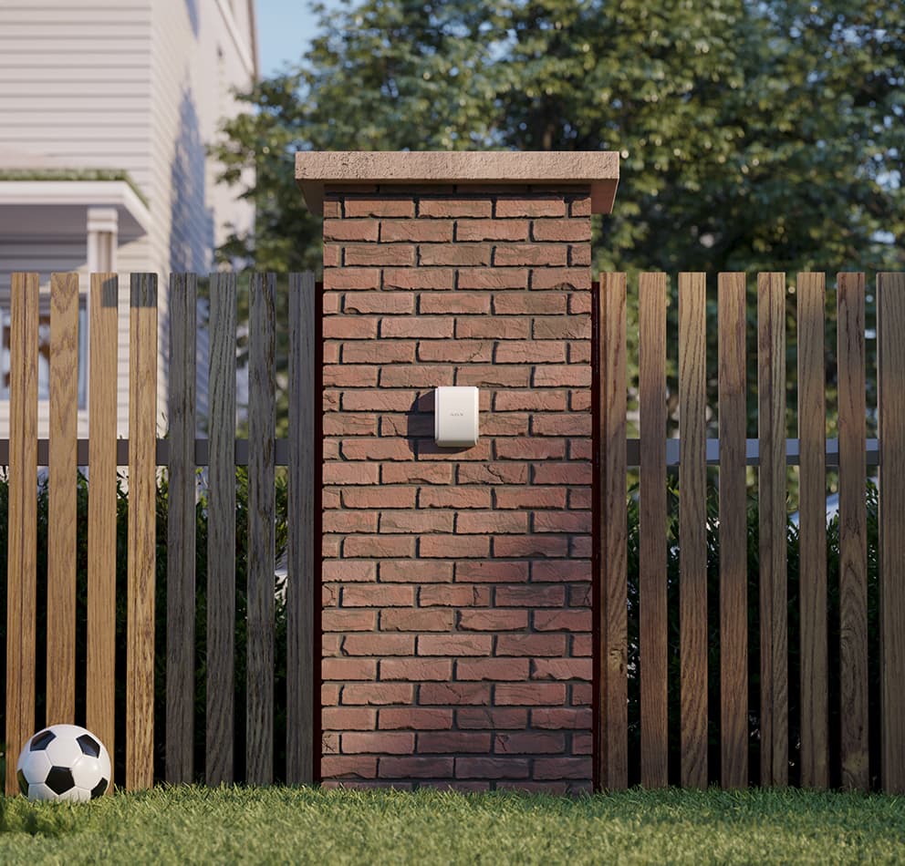 Ajax wireless security sensor installed on residential brick wall with wooden fence - professional home security installation