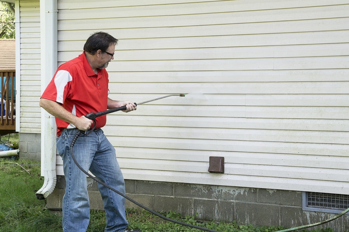 man pressure washing house