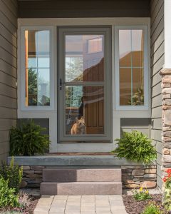 Close up view of the front porch of a home. The entry door has a dark green storm door.