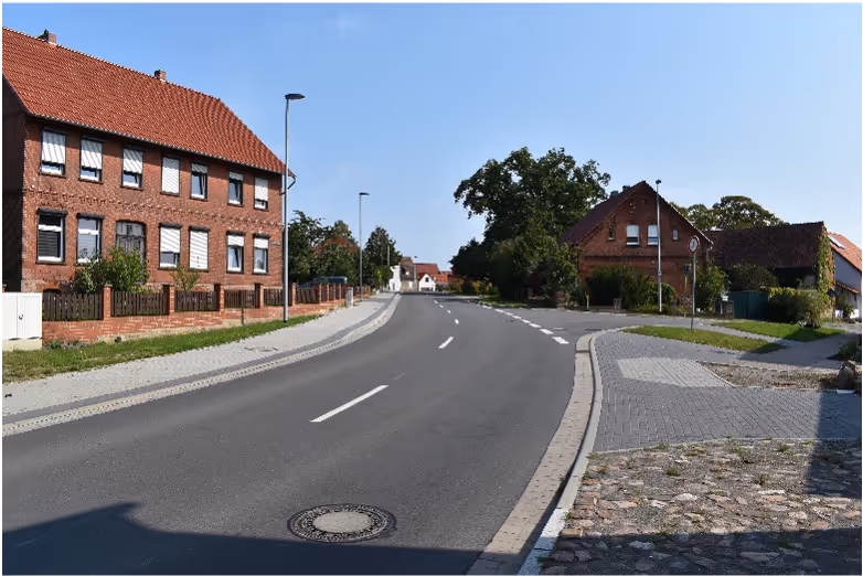 Curved asphalt road lined with brick houses and lamp posts under a clear blue sky.