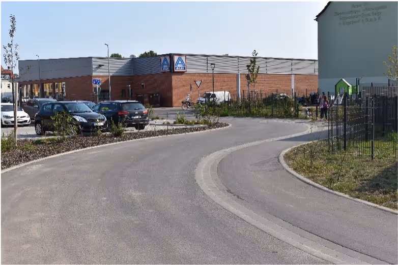 Curved road leading to a parking lot with cars in front of a building with Aldi signs.
