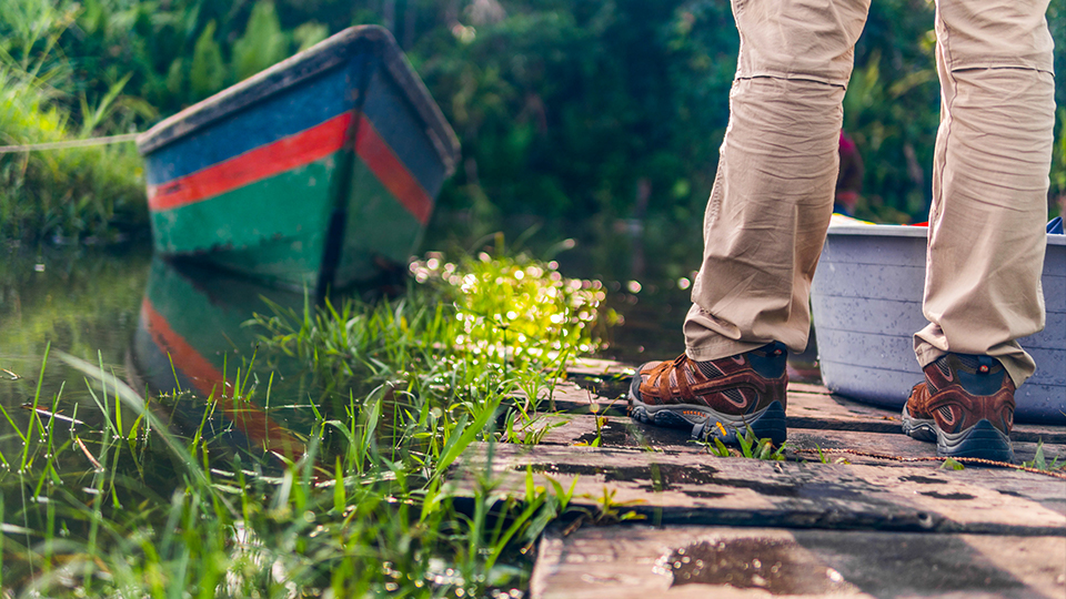 A boat on a river and hiking boots on a wooden dock