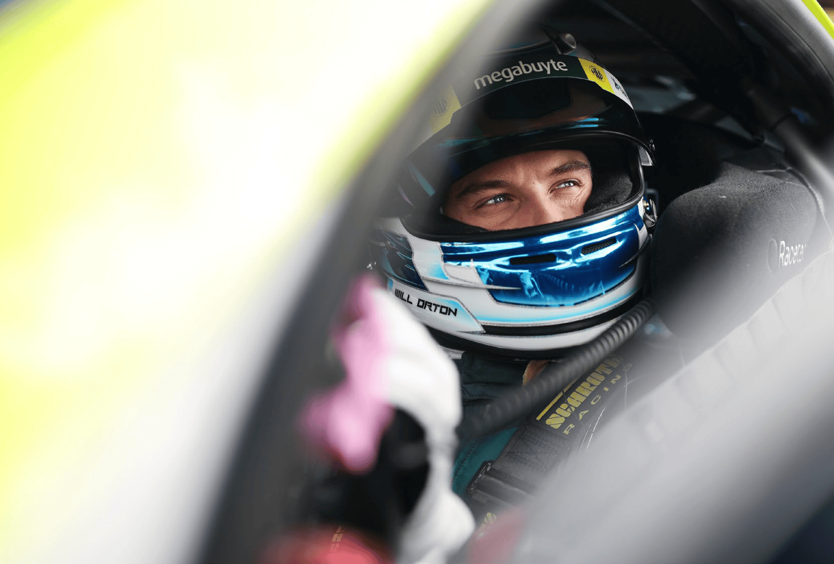 Race car driver wearing a blue helmet and sitting inside a car, preparing for a race.