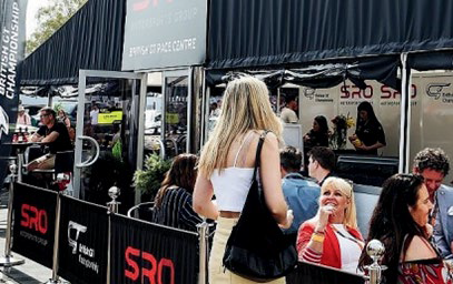 People standing and sitting near an outdoor booth with SRO signage at an event or race.
