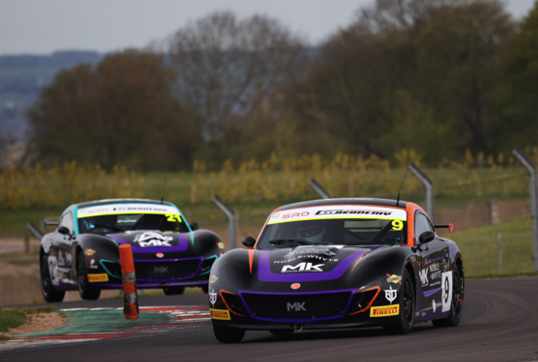 Two black GT race cars with purple accents racing on a track with a green and red curb.