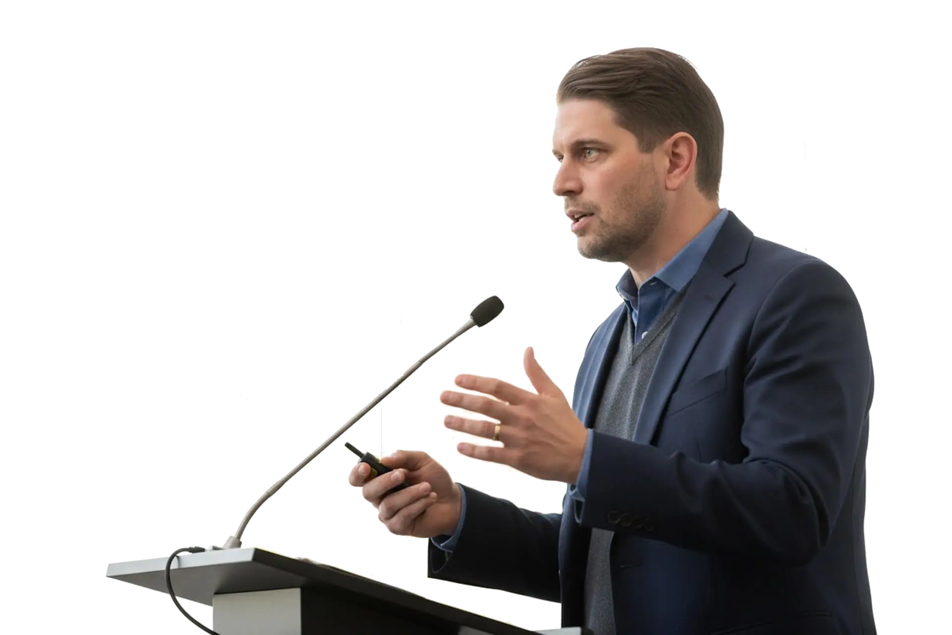 Jay DeVore in a navy blazer and gray sweater speaking at a podium with a microphone.