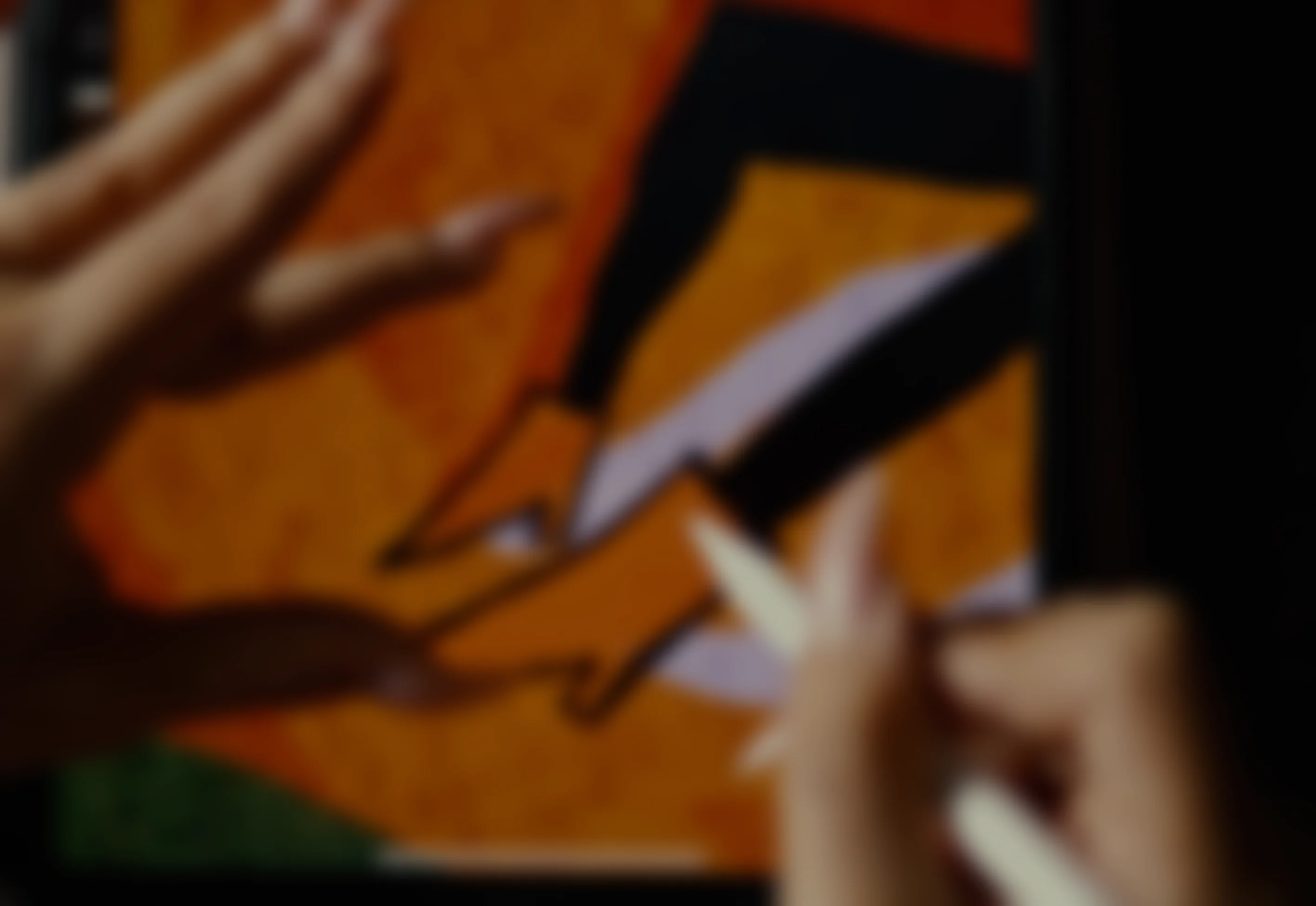 Blurred image of hands working on a tablet with an orange and black drawing or design.