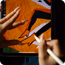 Hands using a stylus to draw orange boots on a digital tablet.