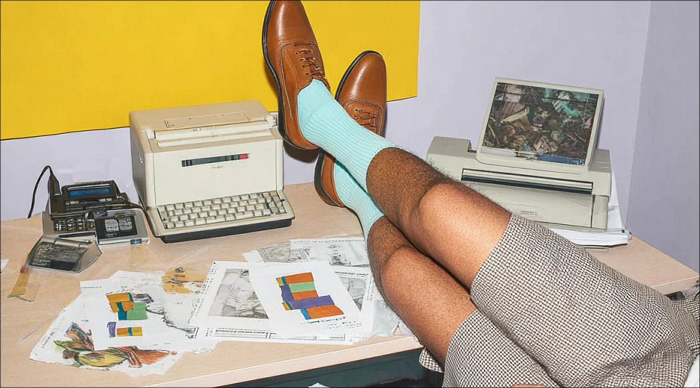 Person with legs crossed on desk wearing brown shoes, light blue socks, and plaid skirt, surrounded by vintage office equipment and papers.