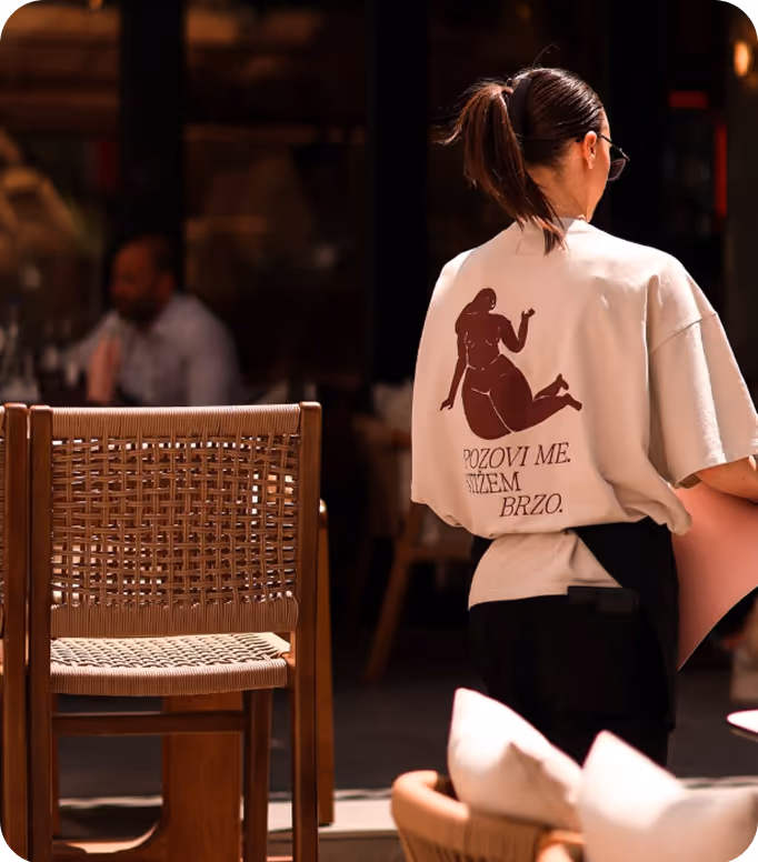 Open menu with a green page listing vitamin juices and prices in Serbian, next to a cartoon black fox wearing red boots holding a glass, on a wooden table with a person's hand nearby.