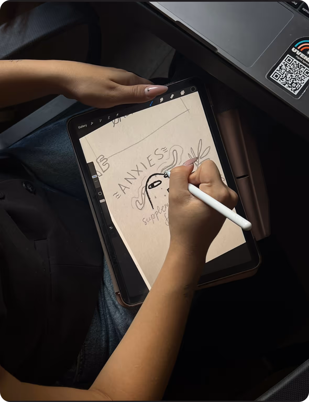 Person using a stylus to draw a digital illustration on a tablet with the word 'ANXIES' and abstract shapes.