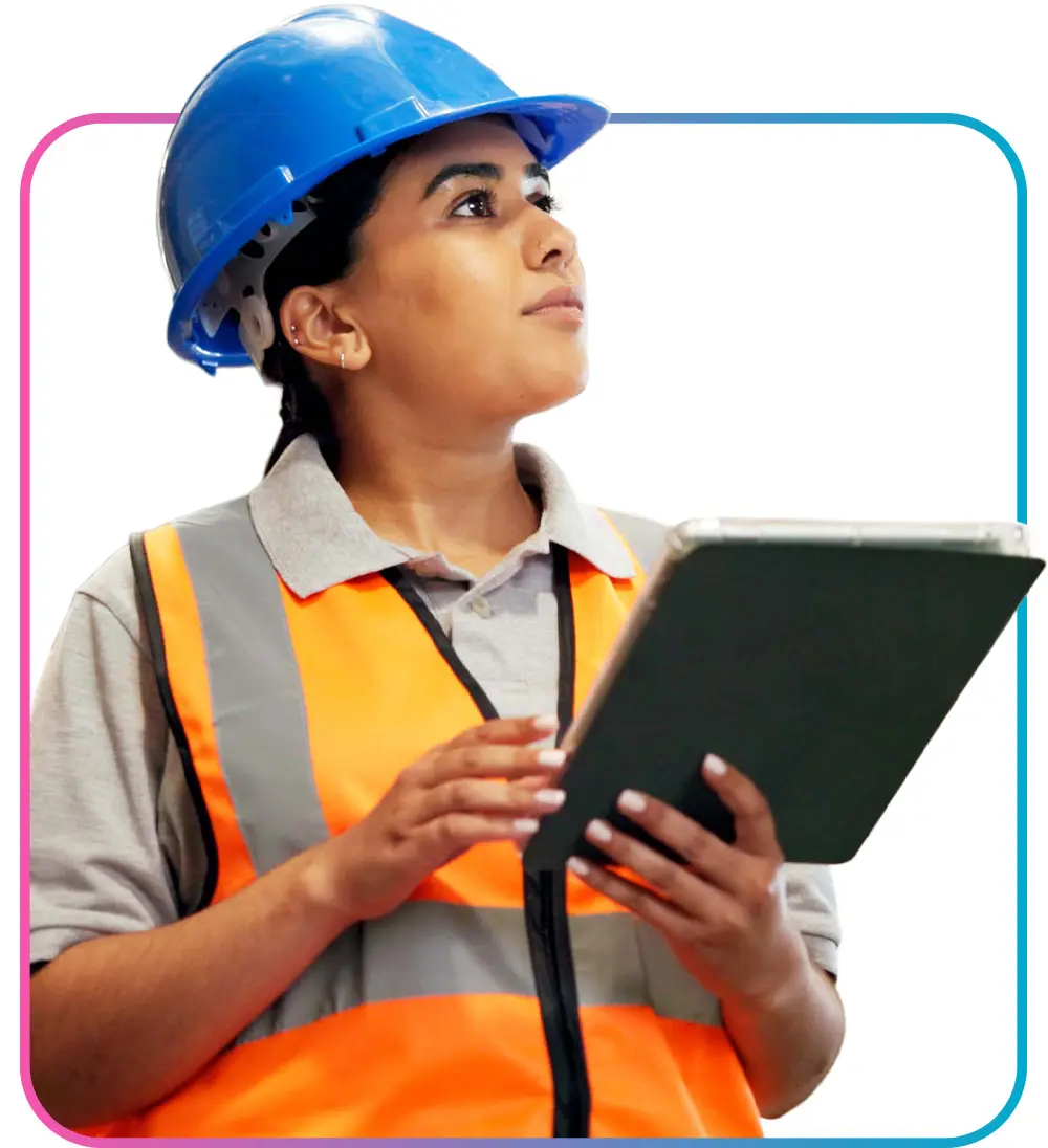 Woman in hard hat and safety glasses holding tablet while looking off to the side