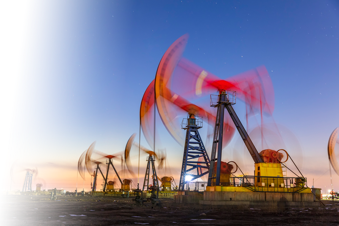 Multiple oil pumpjacks operating at dusk with motion blur on the red counterweights against a clear sky.