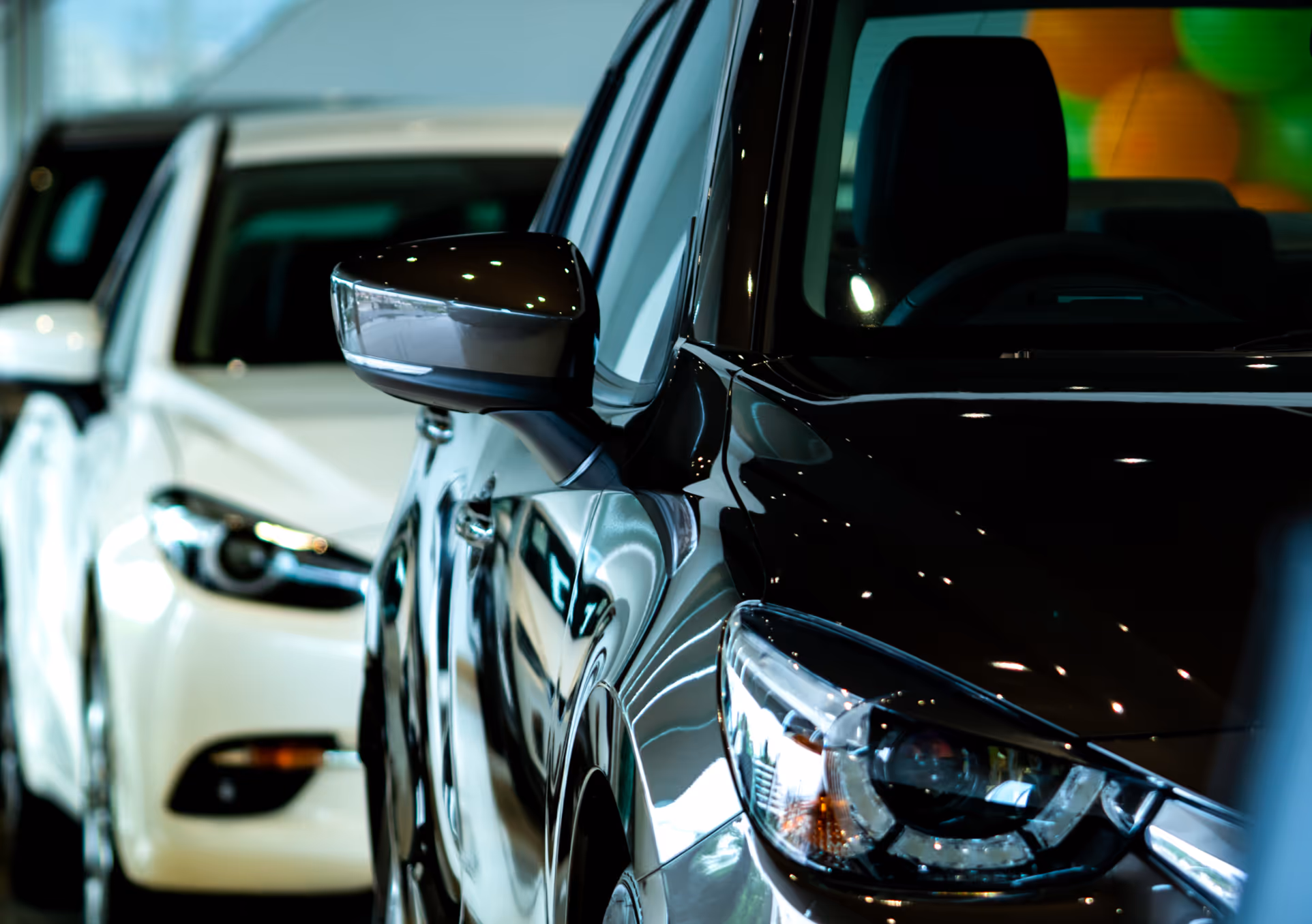 Nahaufnahme von zwei geparkten Autos, vorne ein schwarzes und dahinter ein weißes Auto, sichtbar sind Außenspiegel und Scheinwerfer.