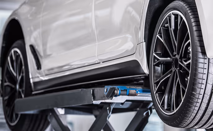 Weißes Auto mit schwarzem Rad auf einer Hebebühne in einer Werkstatt.